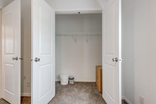 An empty closet with white doors and carpet.